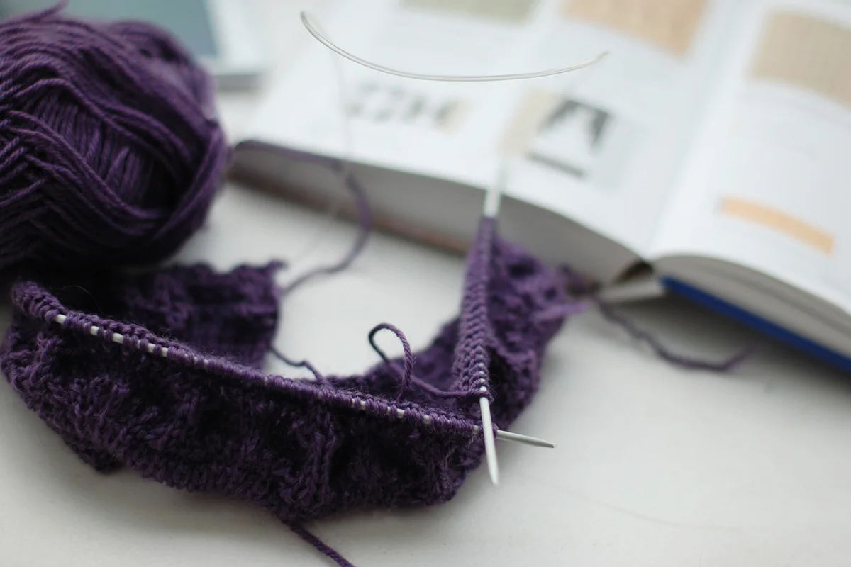 Knitting project in purple color by an open book