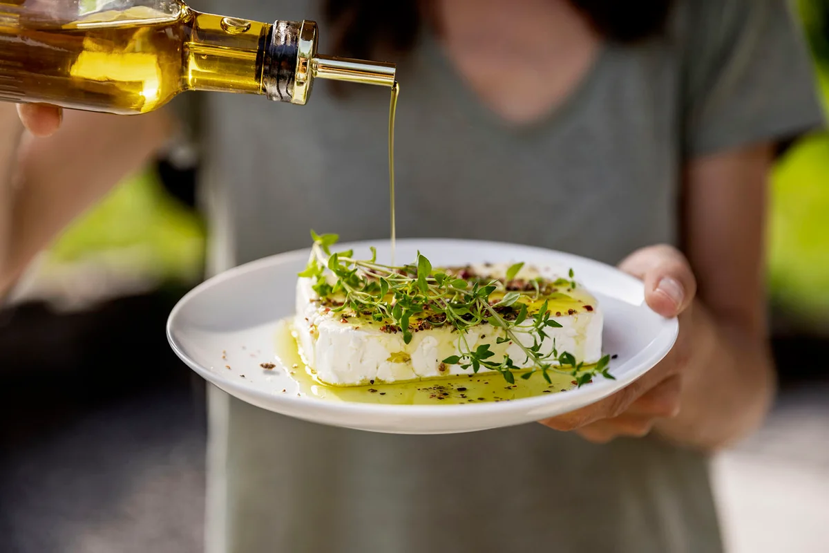 woman pouring olive oil over sheep cheese on plate