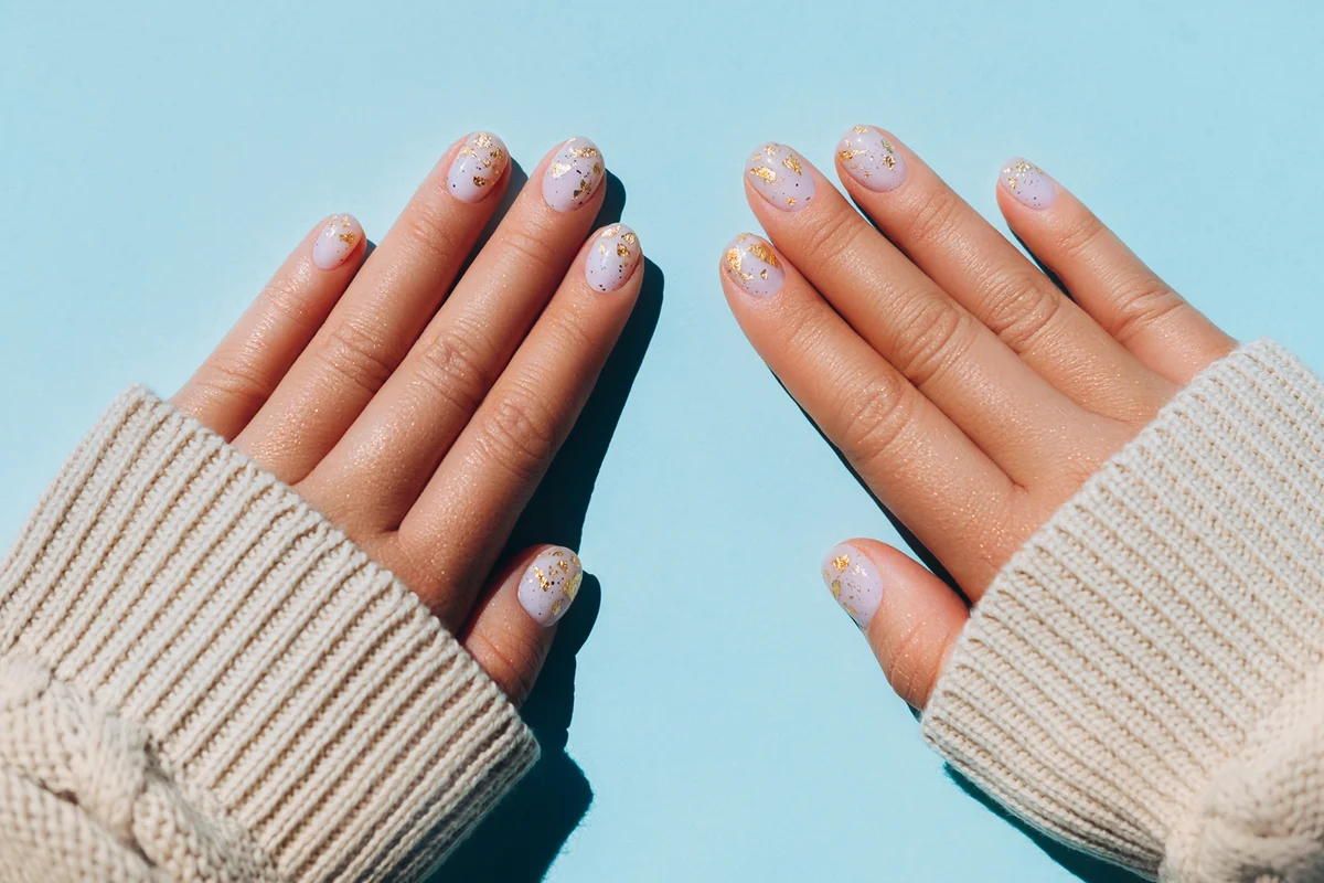 Glowing hands in sweater with knitted sleeves and with nude color manicure with gold particles on blue table