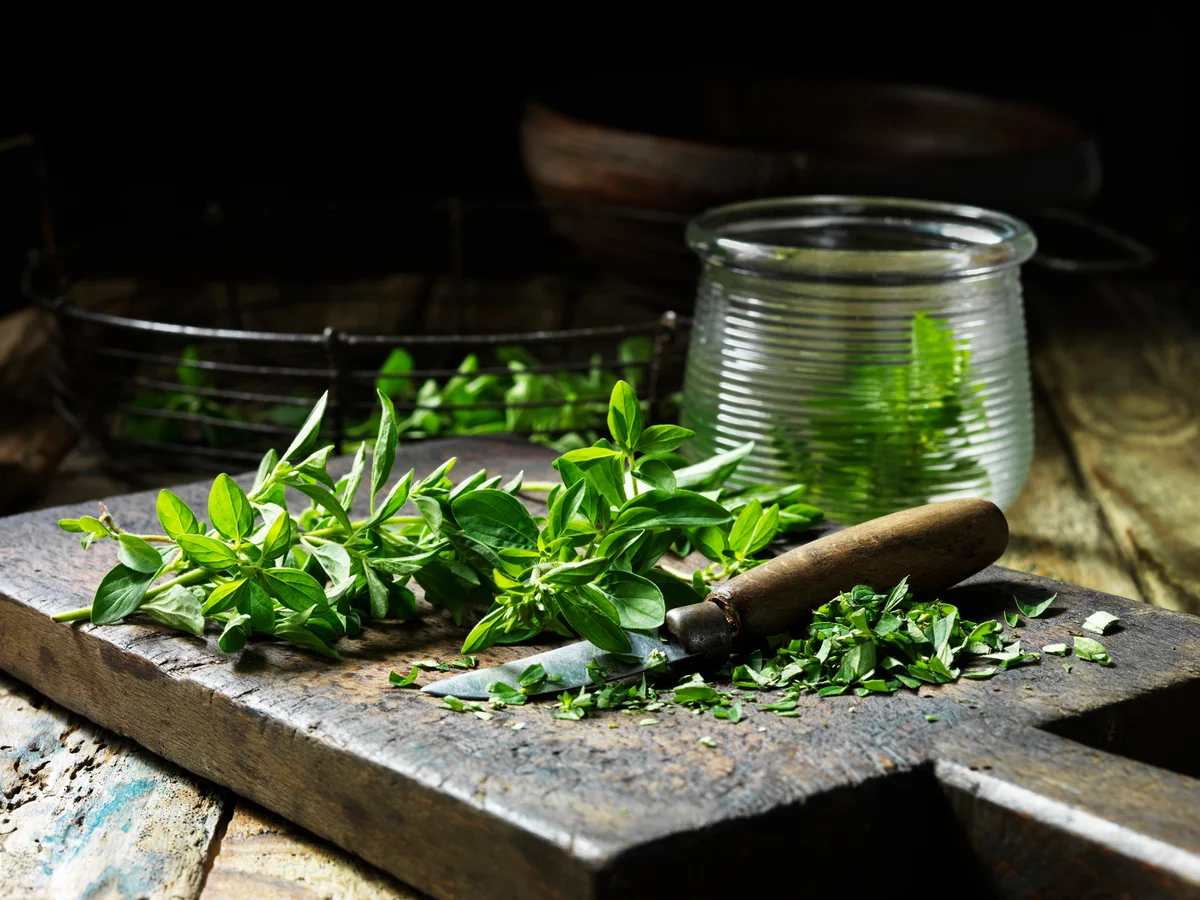 Marjoram, whole and chopped, some in glass jar, vintage knife, rustic wooden chopping board