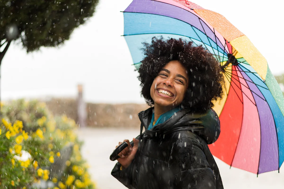 Smiley woman holding a multicolored umbrella during a snow storm