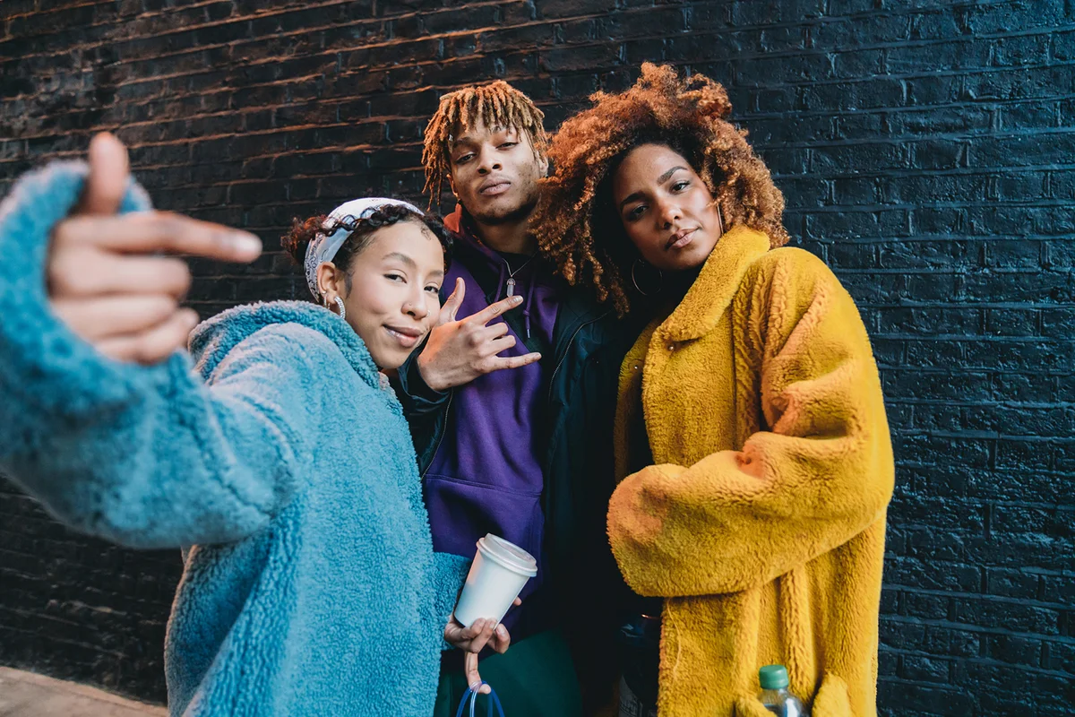 Portrait of three friends against a black bricks wall, making gestures in front of the camera