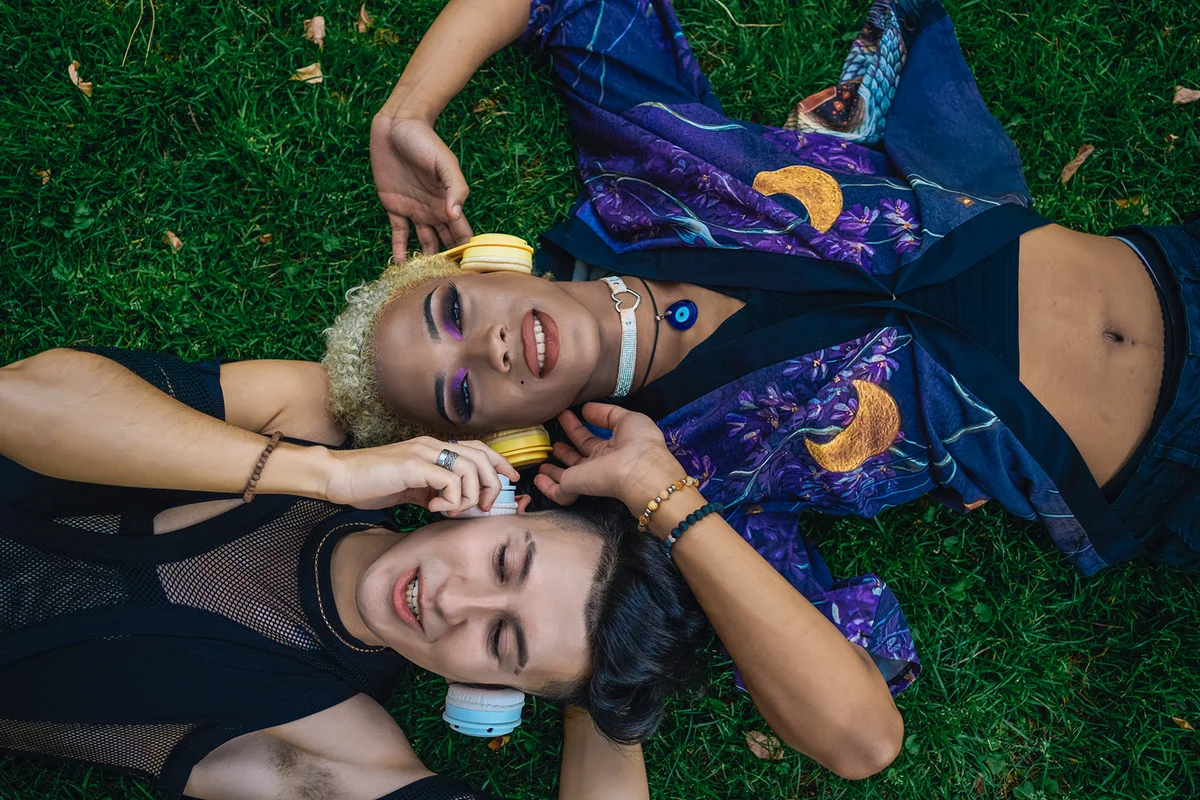 friends lying on their backs on the grass in a park and listening to music