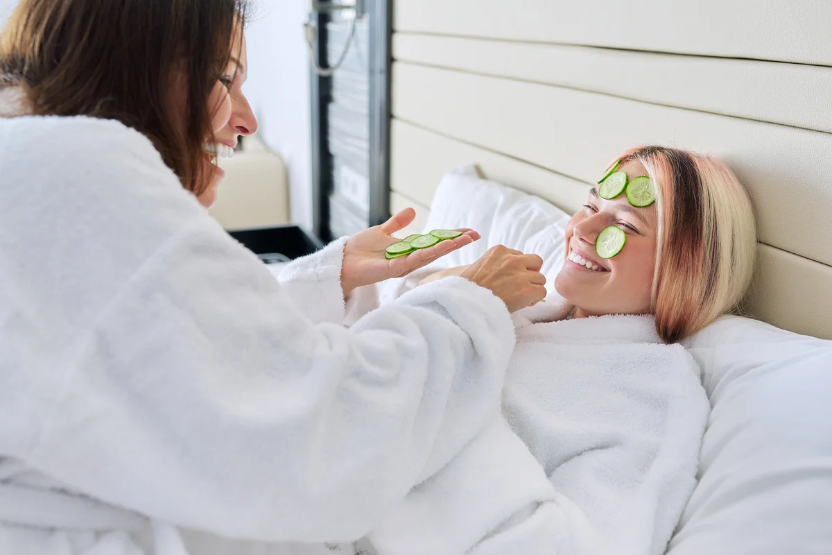 Mom and teenage daughter taking care of face using natural cosmetics and cucumber