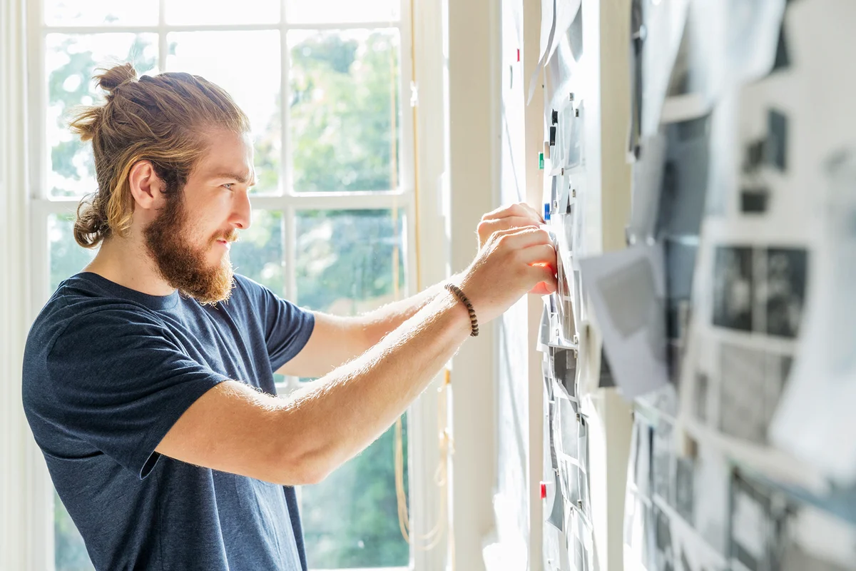 Young male designer pinning mood board ideas to wall in creative studio