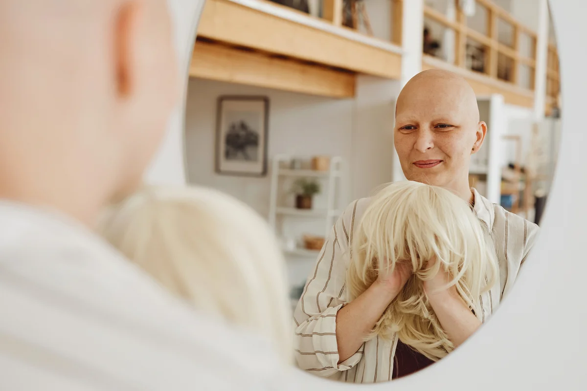 Cancer patient with wig on her hand looking to the mirror