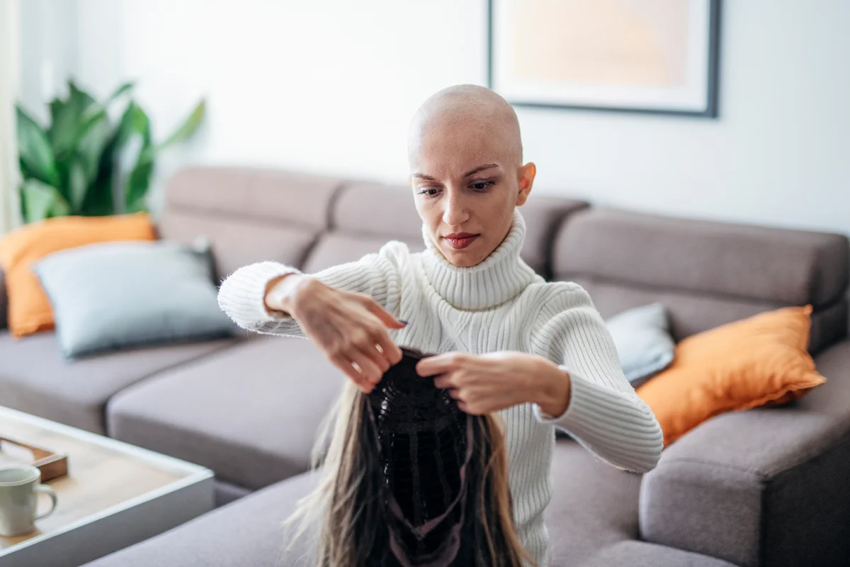 Beautiful woman putting on a wig after hairloss due to cancer treatment.