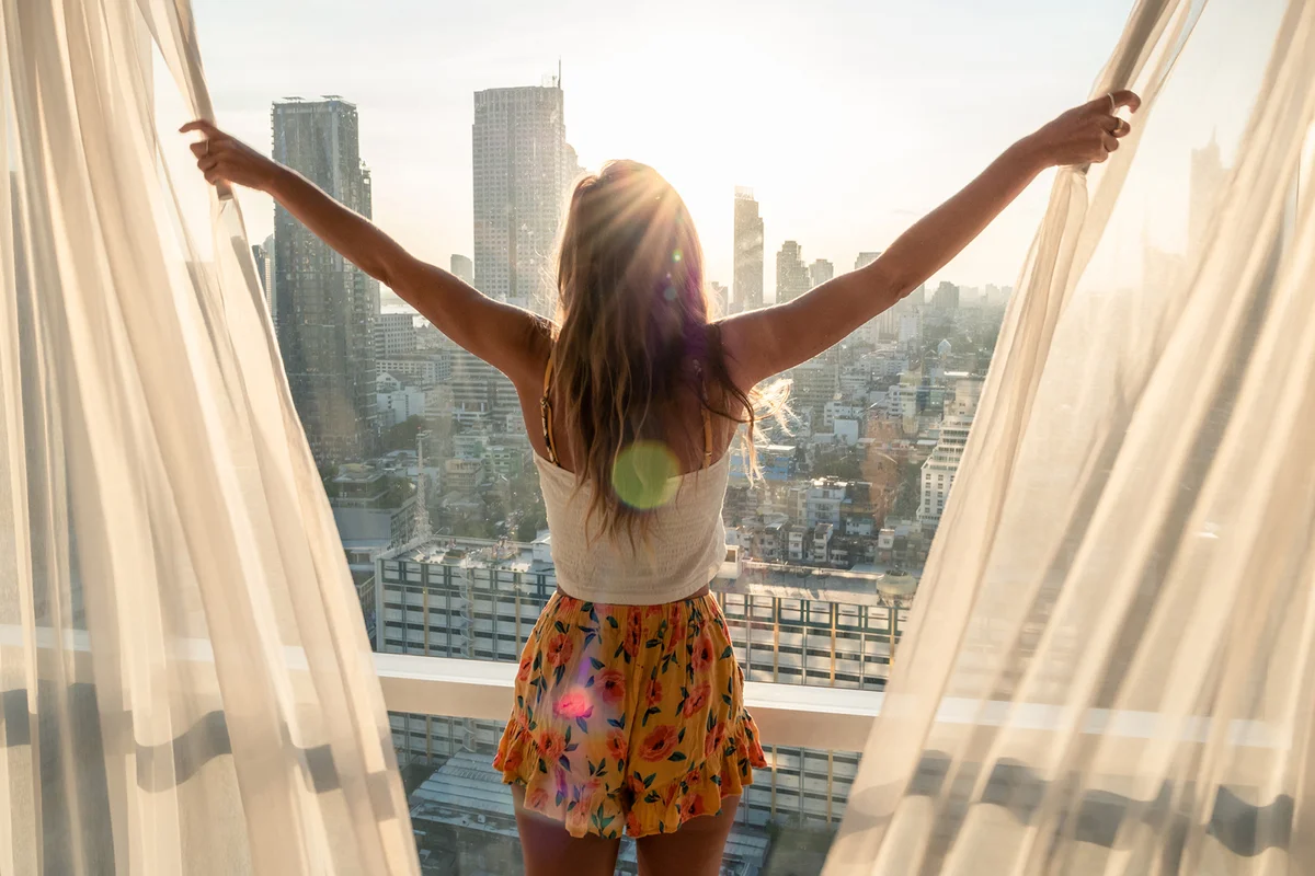 Woman opens curtains in bedroom room at sunrise