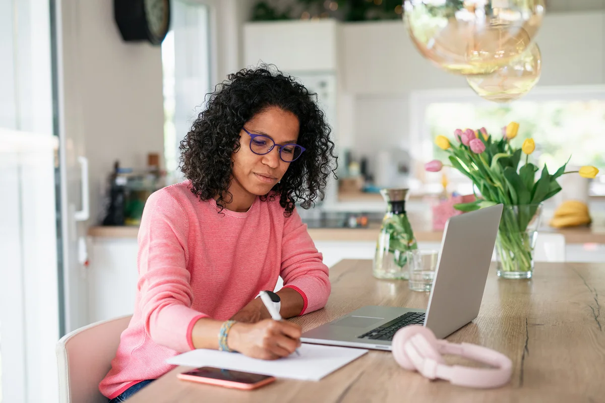 Multiracial woman having home office in kitchen, writing notes