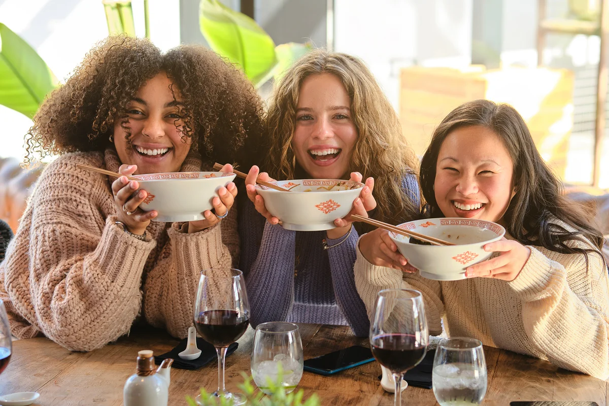Cheerful diverse female friends eating soup together in cafe