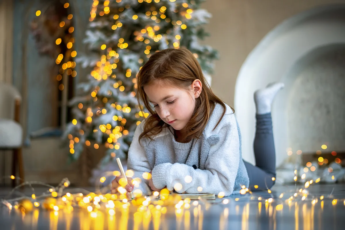 Girl lies on the floor near the Christmas tree and writes on a notepad