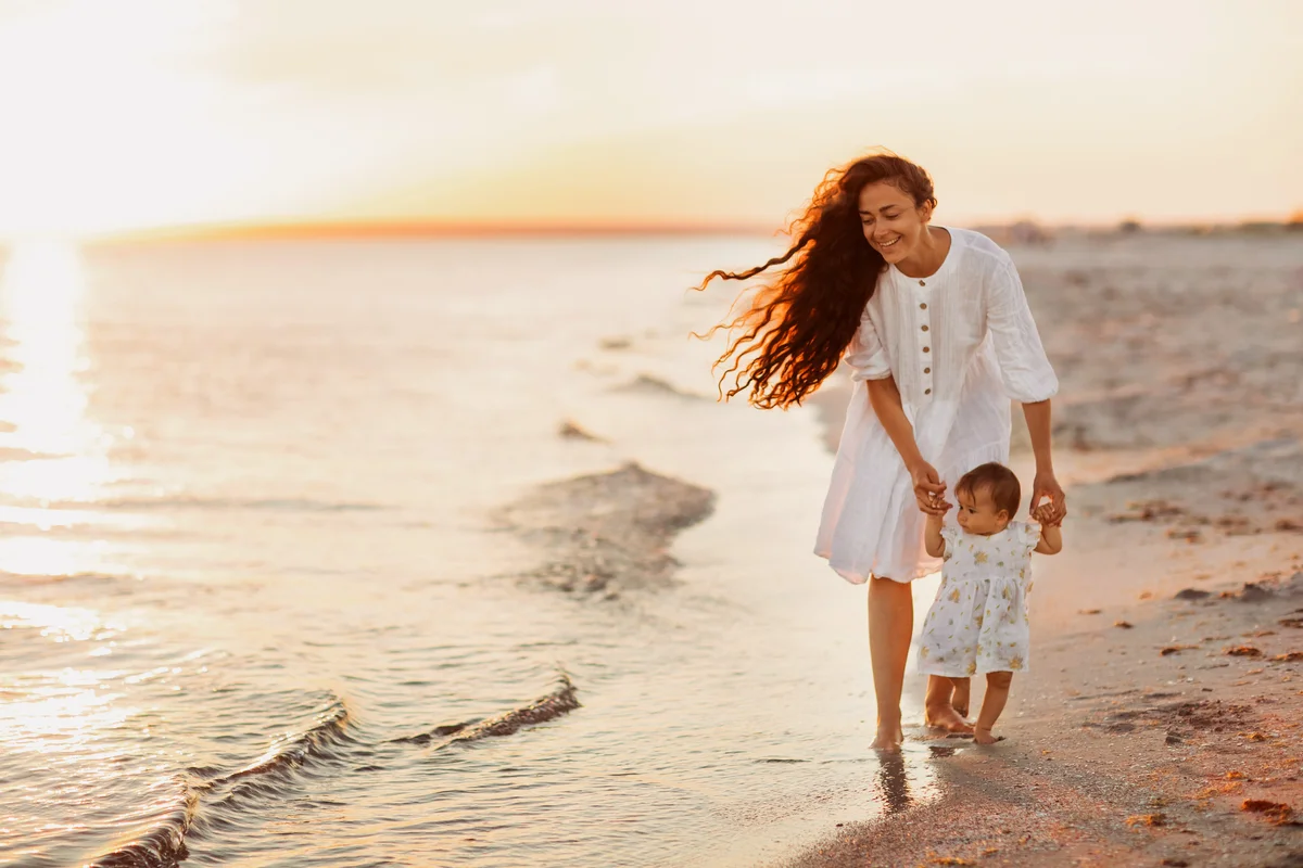 Mother and cute baby walking barefoot along a white sandy beach