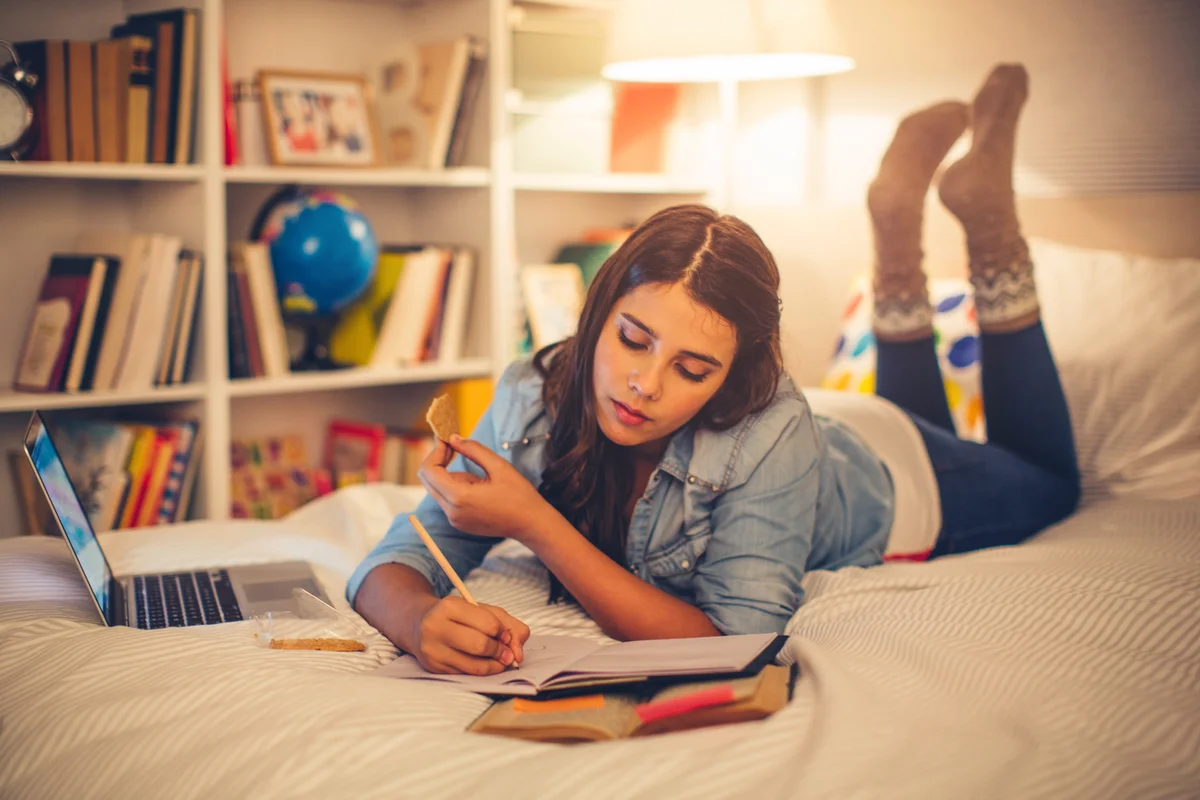 Teenage girl lying on bed in her room and studying at night time