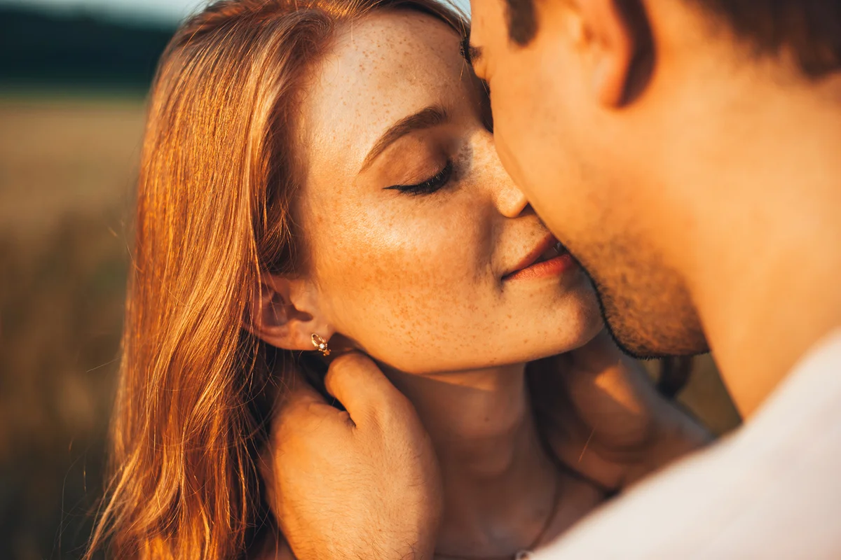 Close-up portrait of a freckled girl kissing her boyfriend while they are on an outdoor date