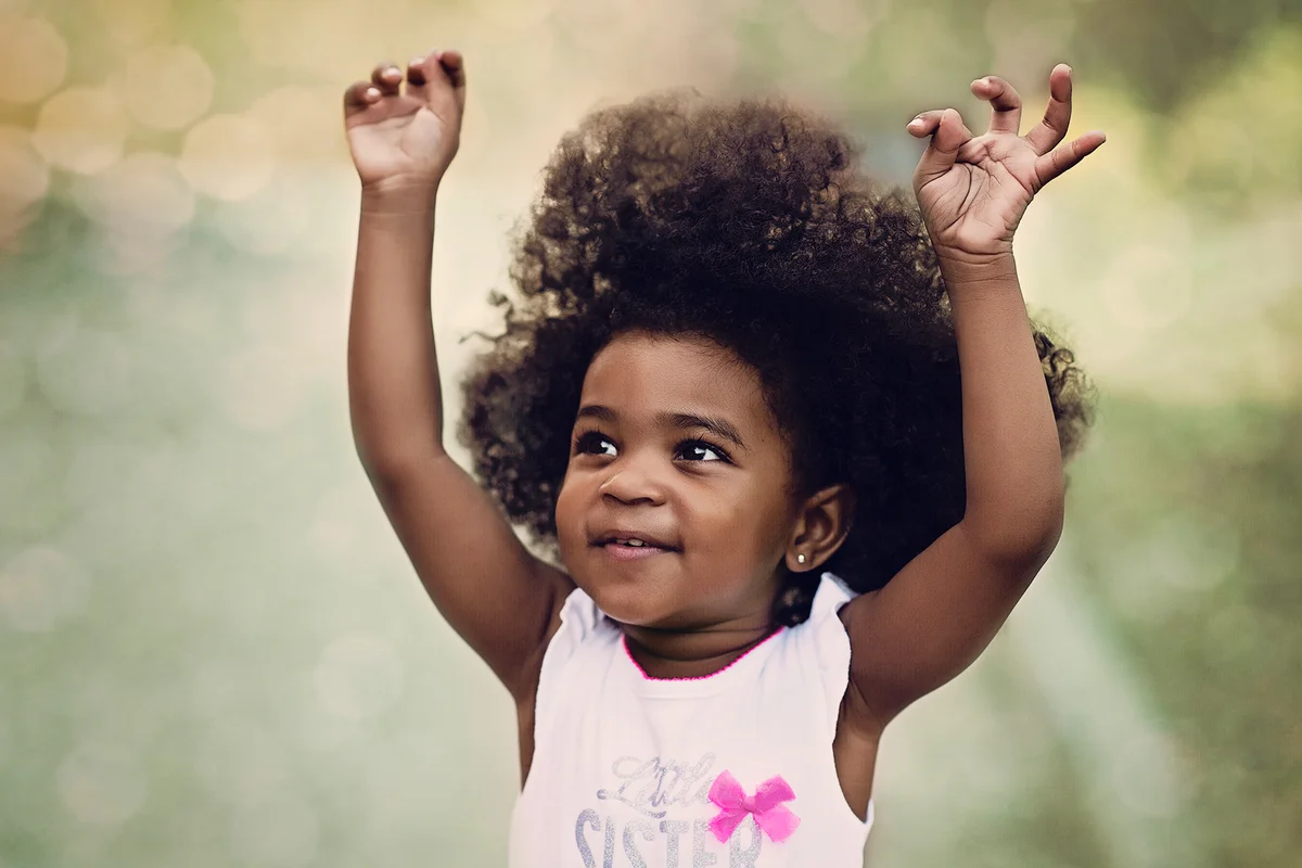 Happy girl toddler with afro outside running and snapping her fingers in the air.