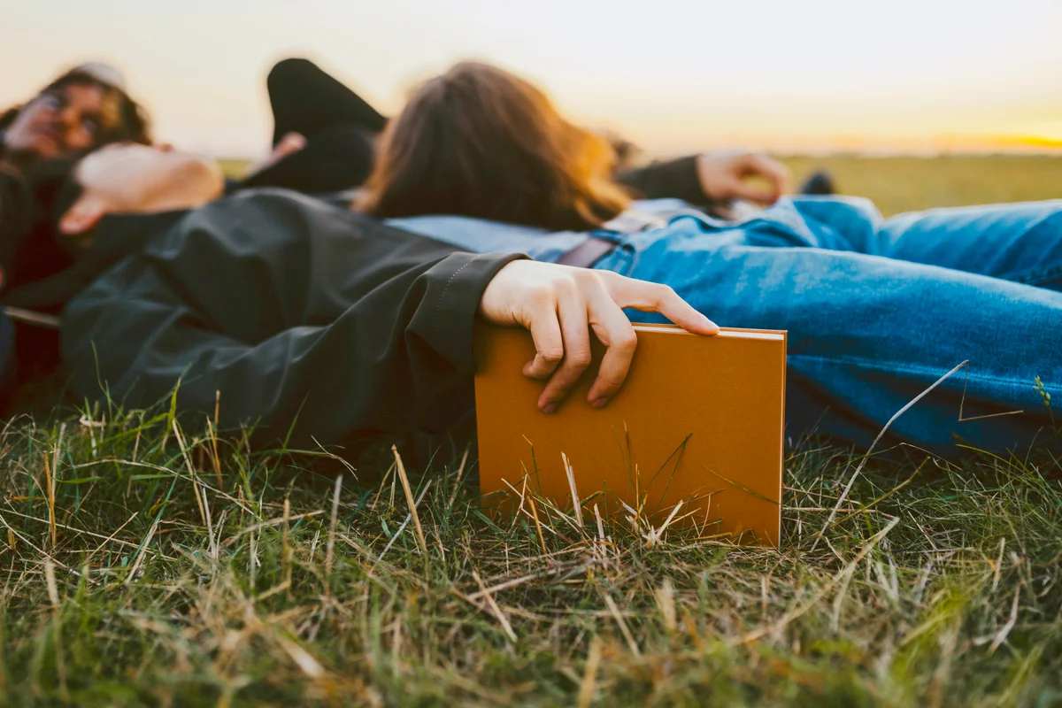 Young man holding diary lying by friends on grass during sunset