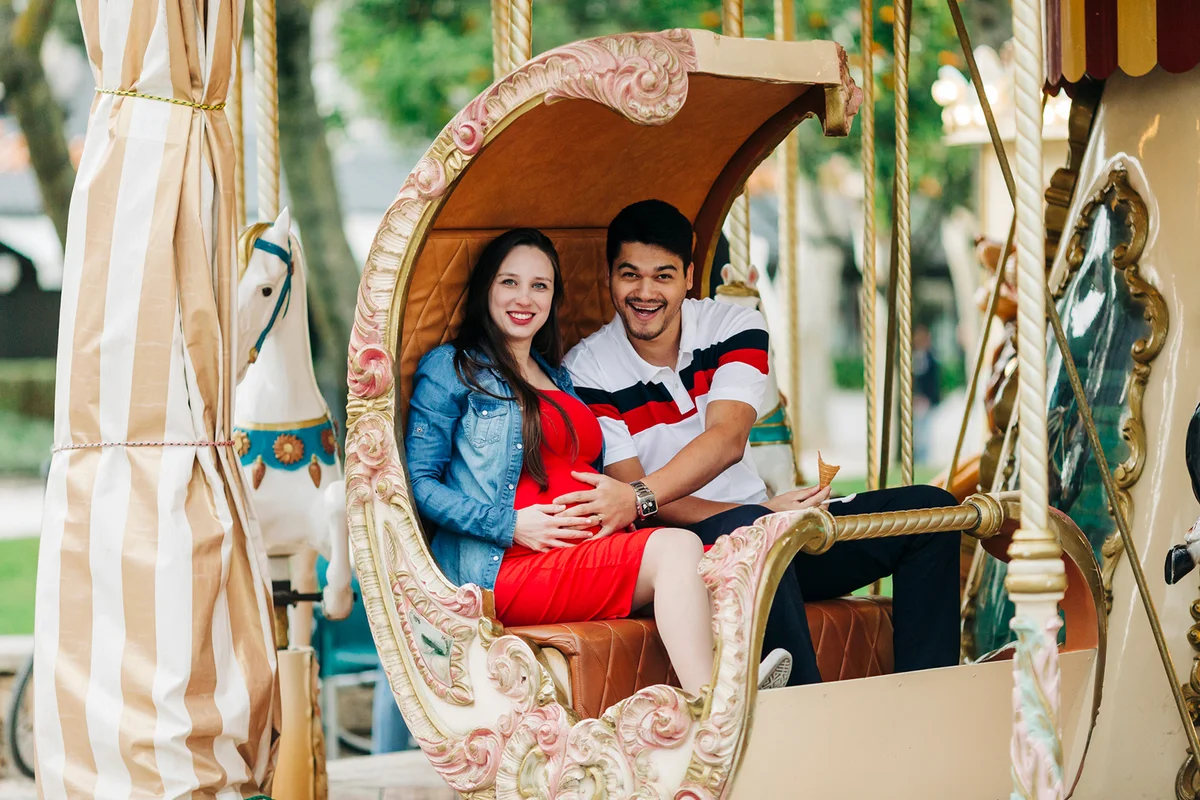 Happy expectant couple sitting on carousel at amusement park