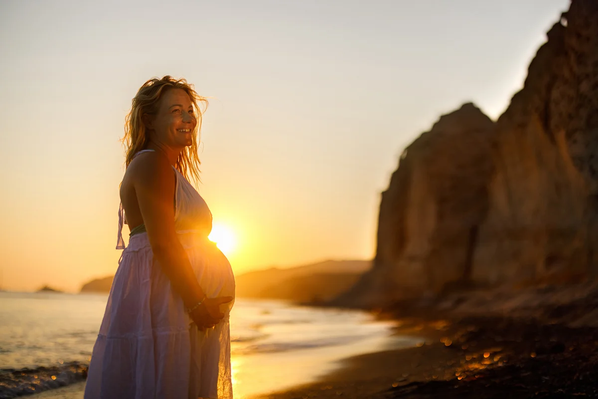 Happy pregnant woman enjoying on the beach at sunset.
