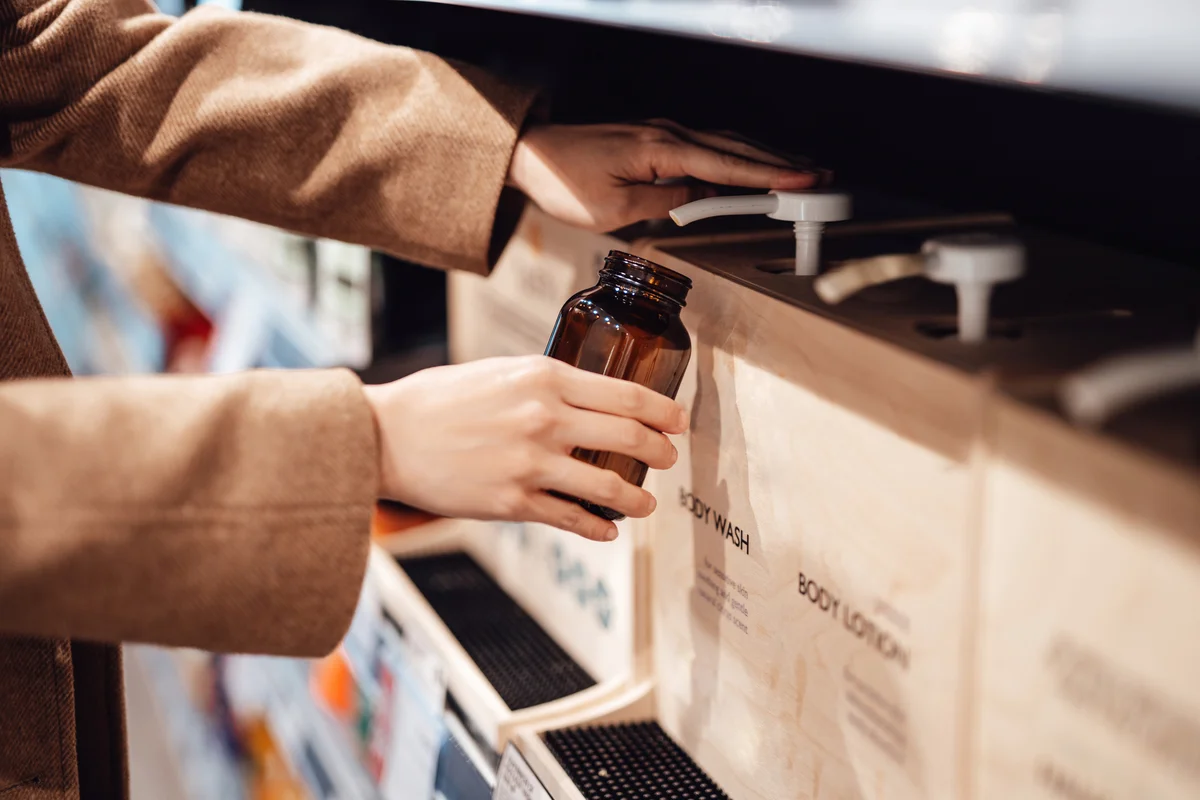 Young woman refilling shower gel into a reusable glass bottle in zero waste store