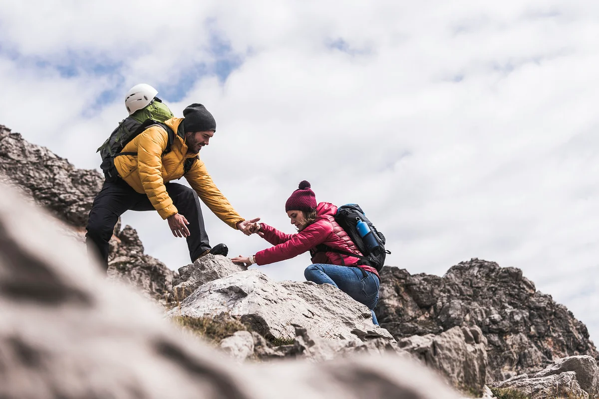 man helping woman climbing up rock