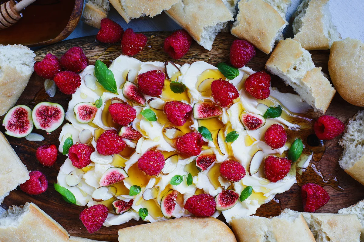 Flatlay of Butter board topped with fresh raspberries, figs, sliced almonds, basil leaves