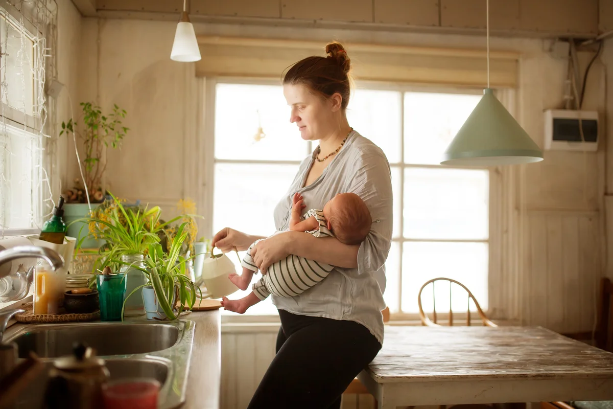 Woman mother holding her newborn baby while trying watering plants at home