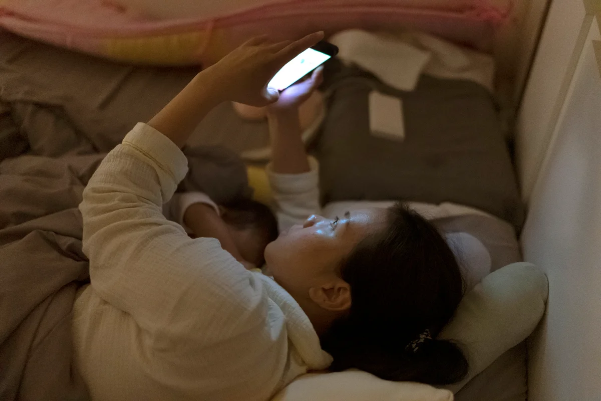 Mother breastfeeding and using phone on the bed