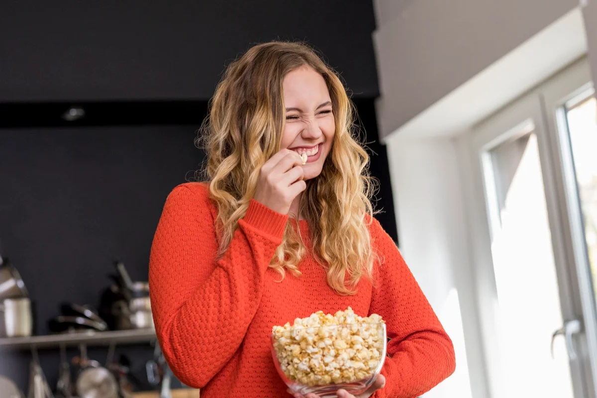 Portrait of giggling young woman with bowl of popcorn in the kitchen