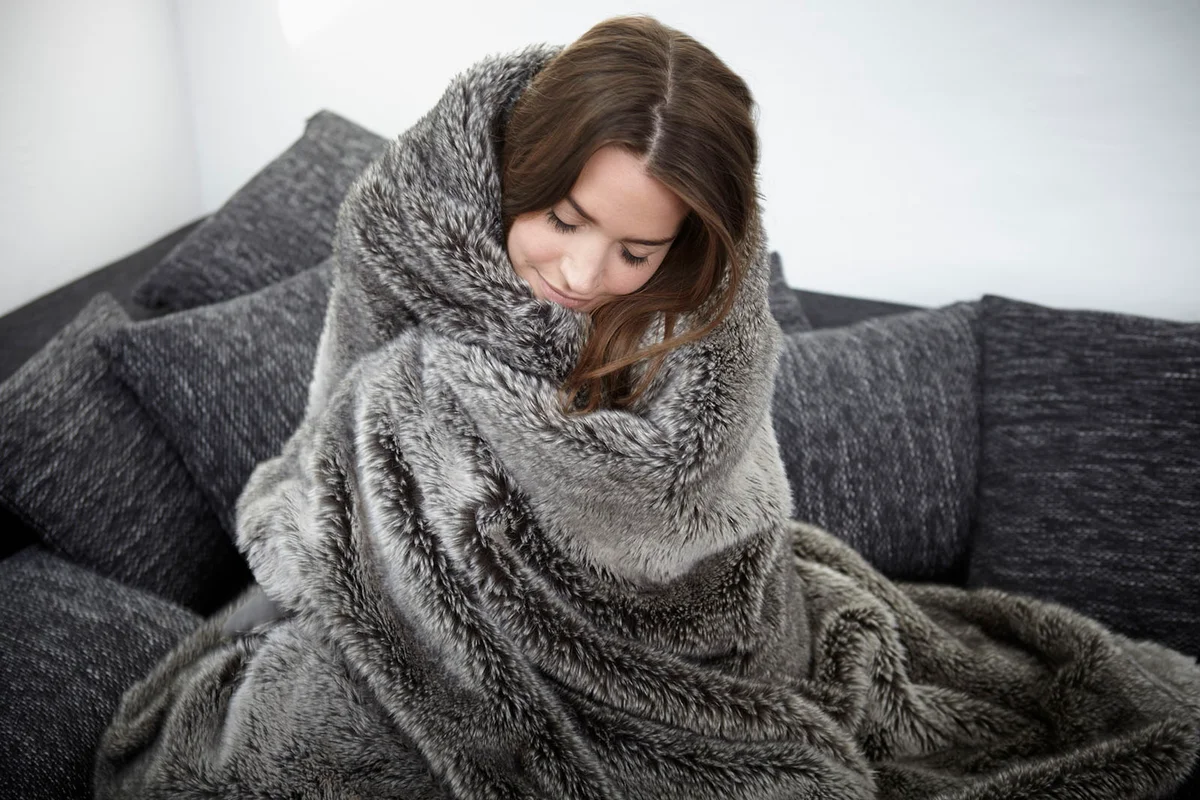woman on couch wrapped in fur blanket