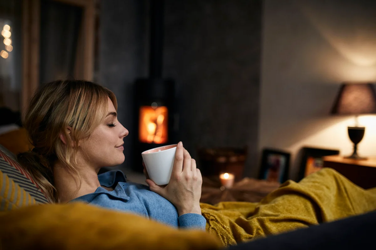 woman with cup of coffee relaxing on couch at home in the evening