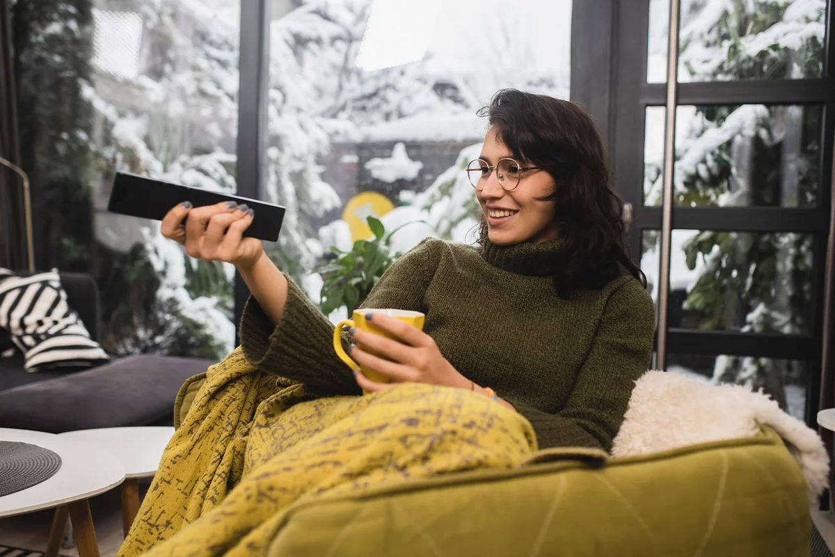 Young woman enjoying coffee and watching TV at home