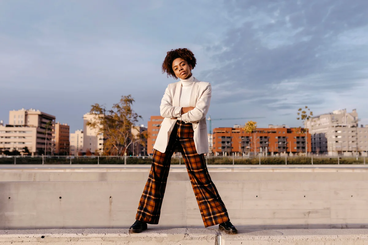 Fashionable woman with arms crossed posing on retaining wall against buildings in city