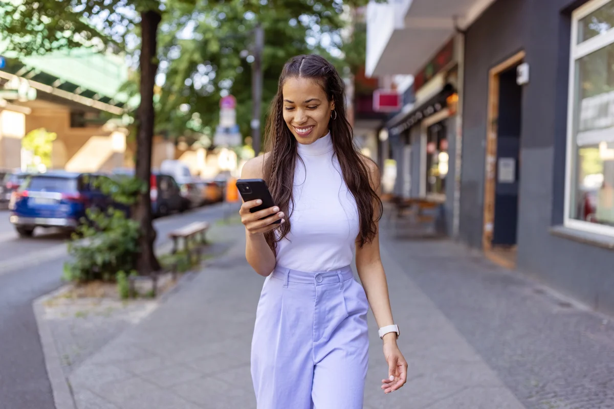 Young woman in casual lilac clothes using her mobile phone on city street