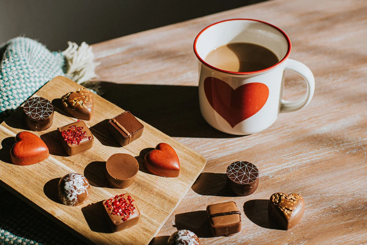chocolates on wooden surfaces beside a cup of hot Coffee