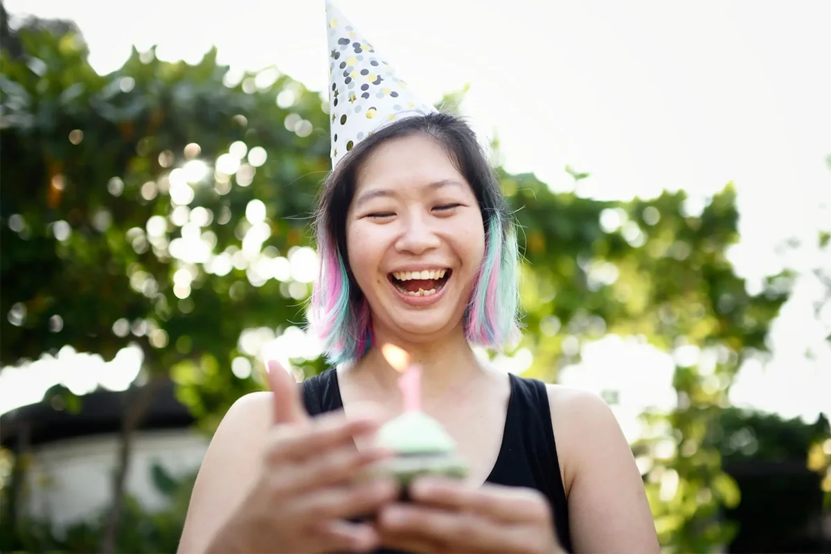 Woman holding a birthday cupcake wearing a party hat