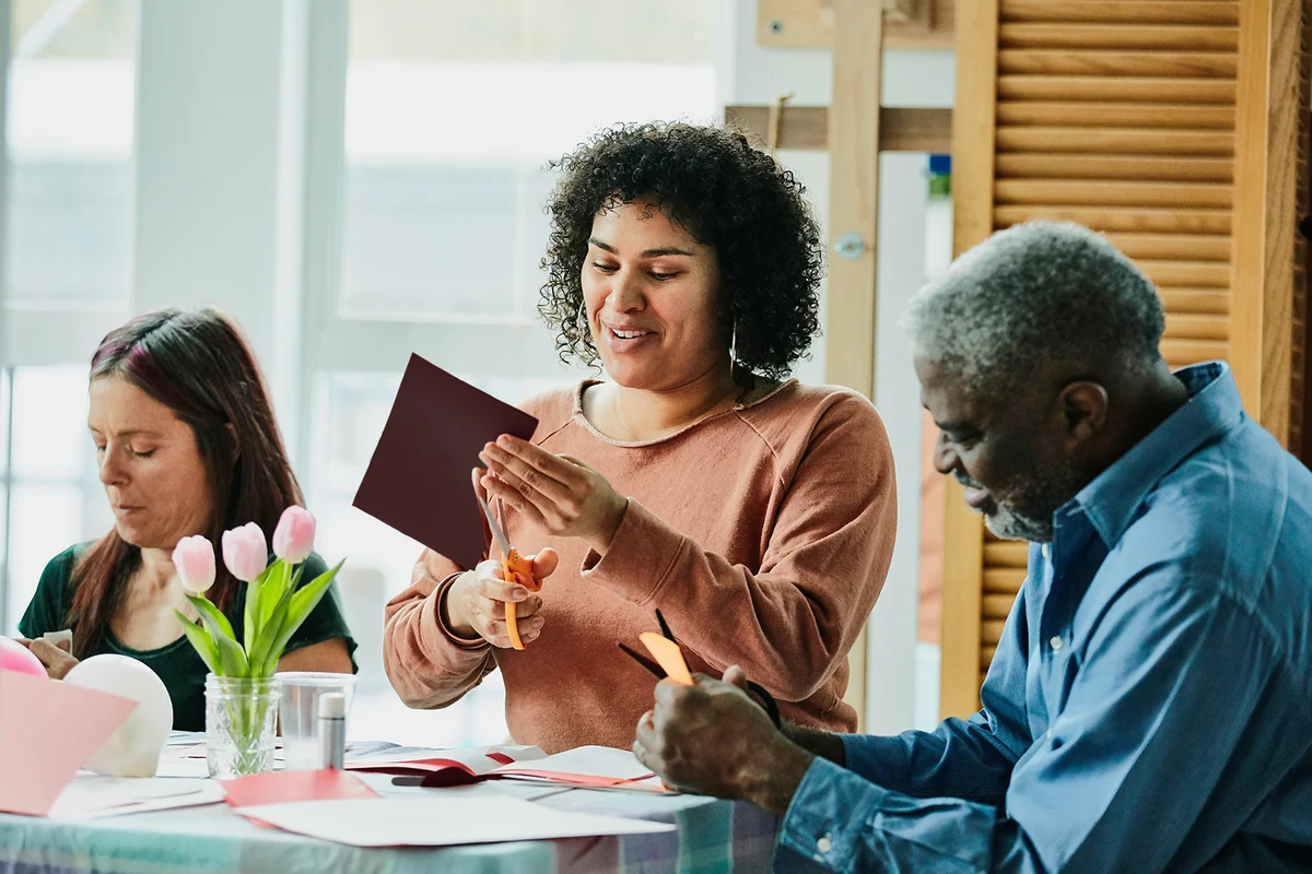 Smiling woman in discussion with father and friends while cutting out Valentines Day card