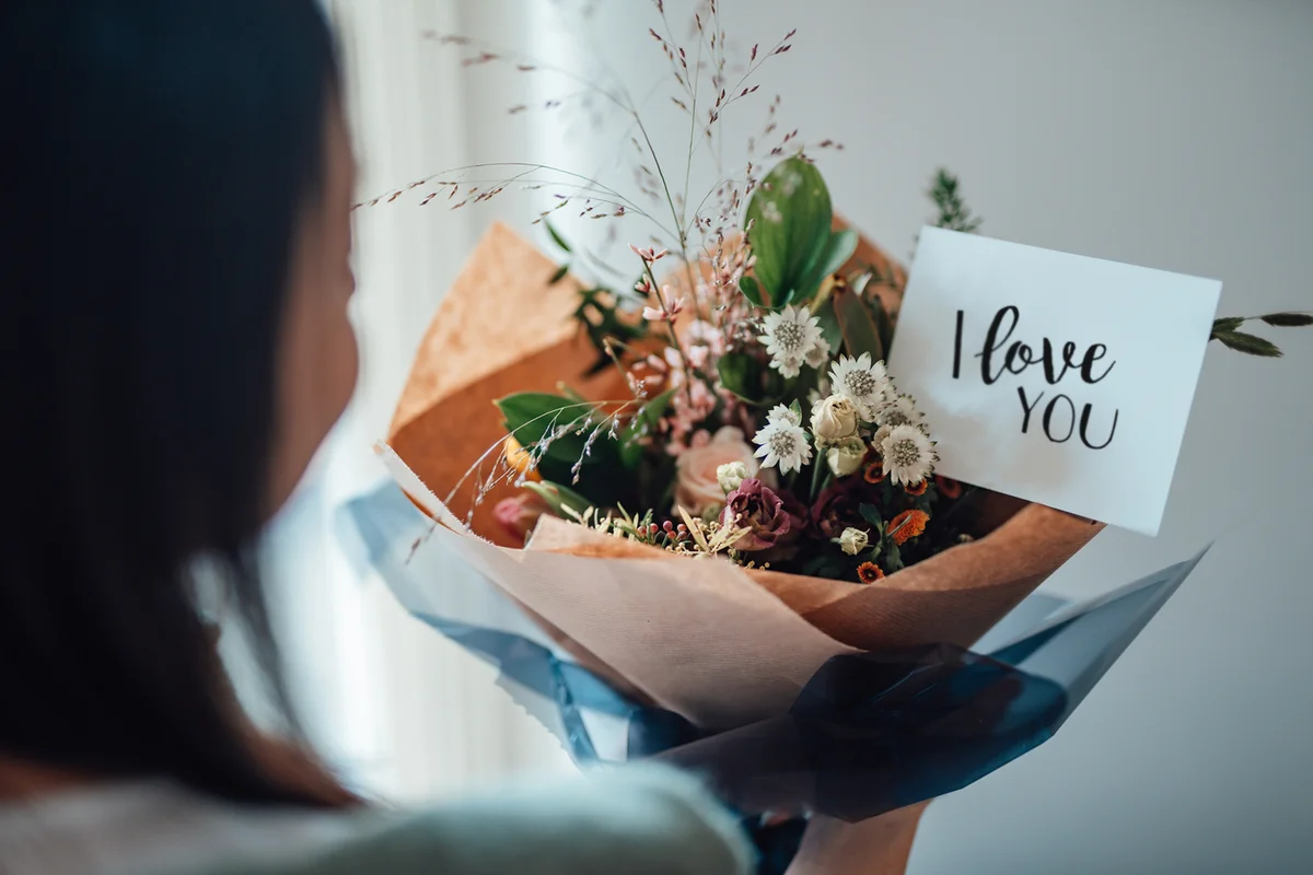 woman receiving flower bouquet with greeting card written "I love you"