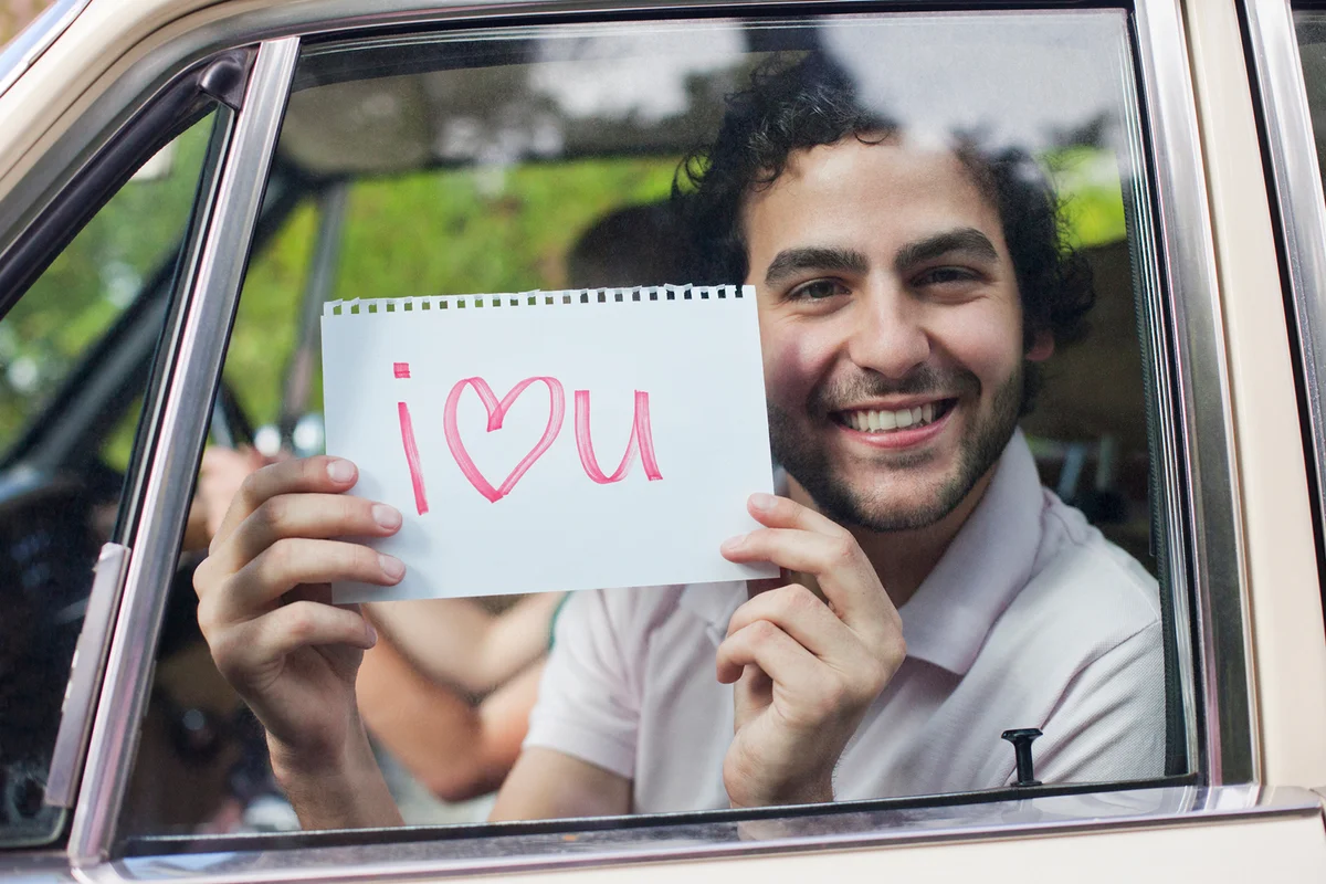 Man in car holding sign saying 'I love you'
