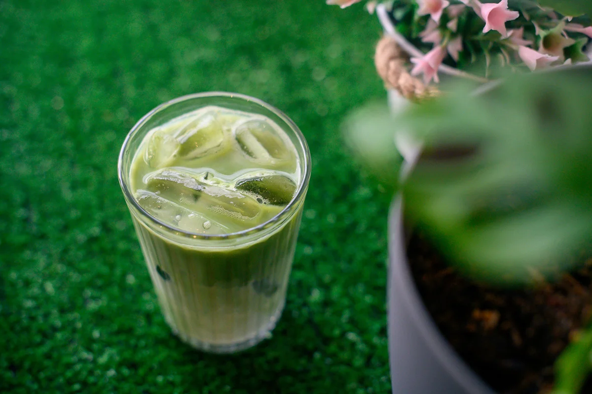 A cup of iced matcha latte on green colored mat
