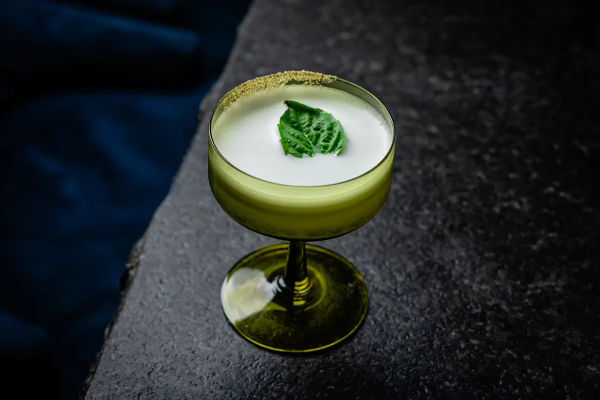Green Cocktail Served in a Coupe Glass and Garnished with a Fresh Basil Leaf