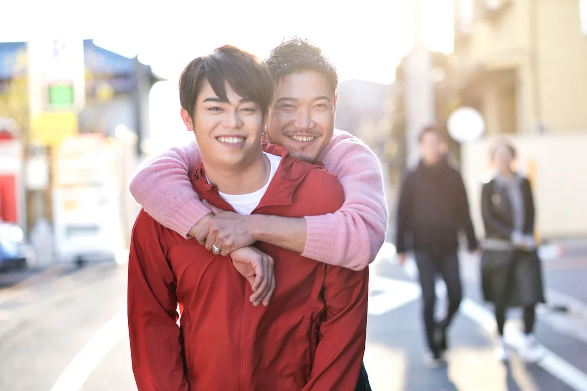 A couple of men looking at the camera while embracing