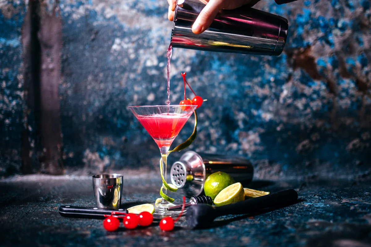 Someone off frame pouring a cosmopolitan cocktail into a martini glass.