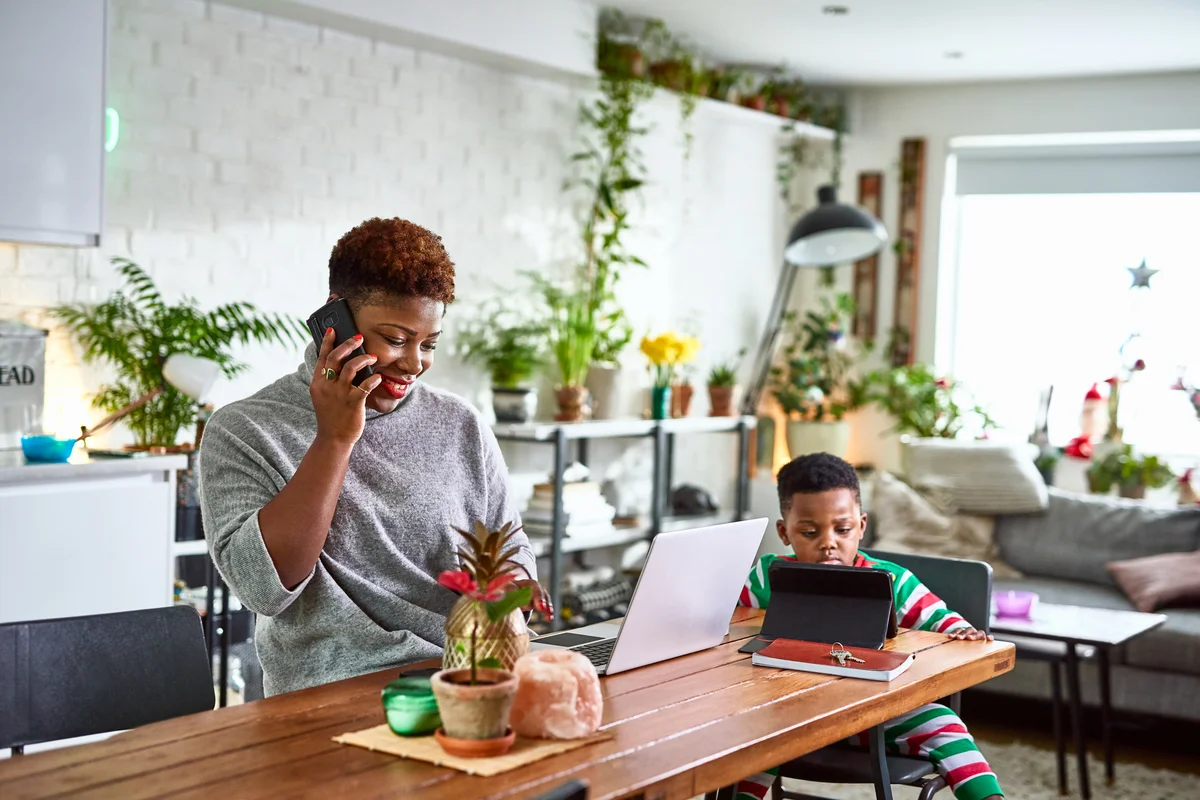 Mother on phone with laptop at dining table and son using a digital tablet