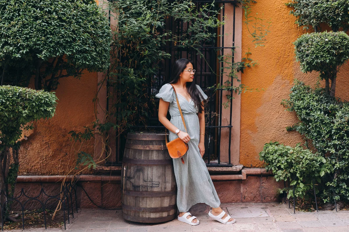 Woman in maxi dress standing in front of yellow wall with plants