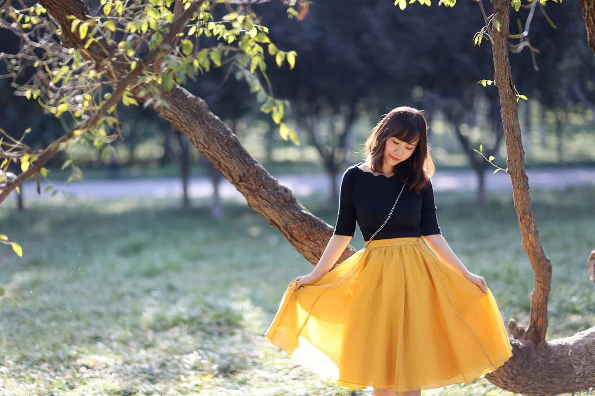 A young lady is lifting her skirt in front of a tree