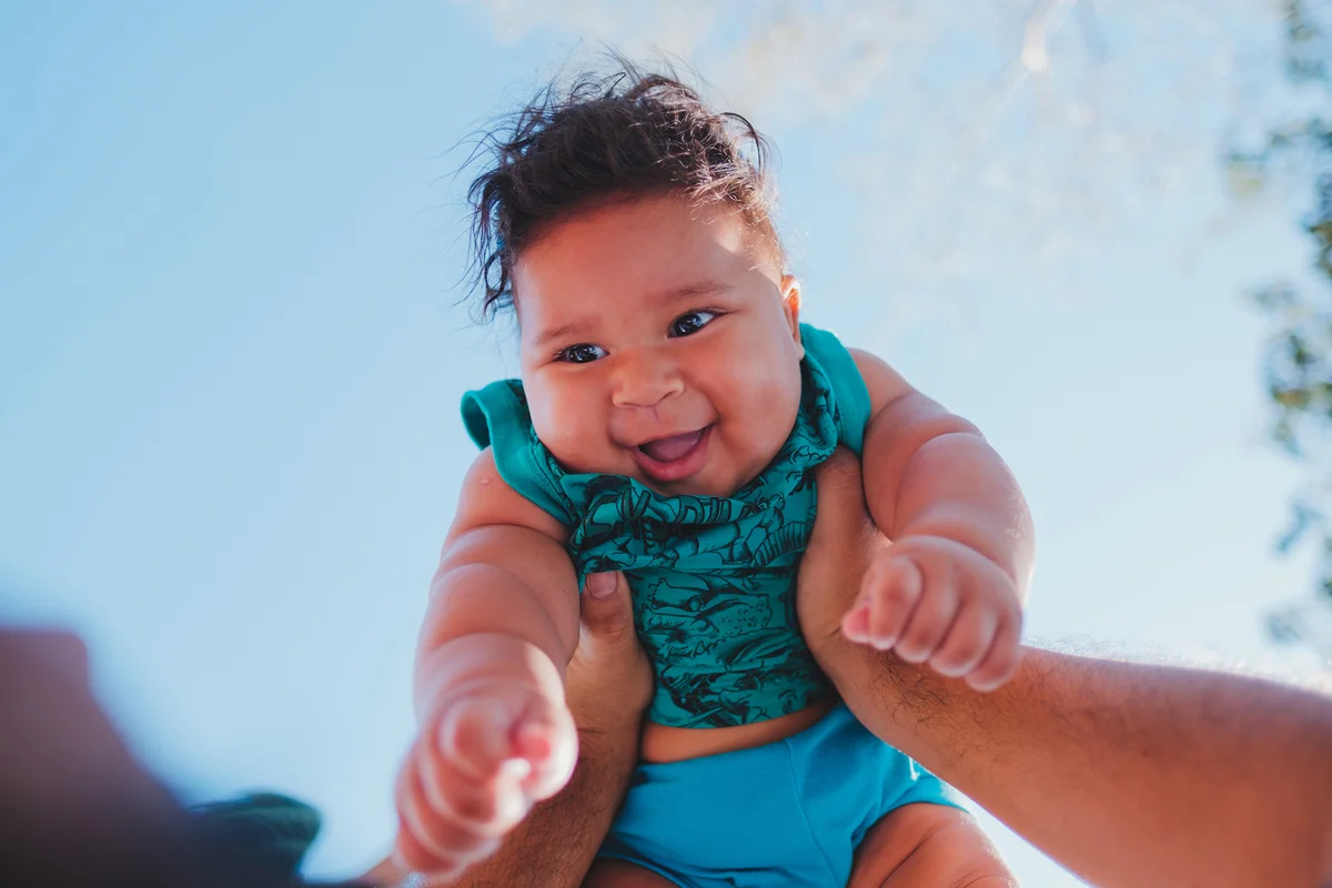 Cropped hand of father carrying cute baby boy against sky