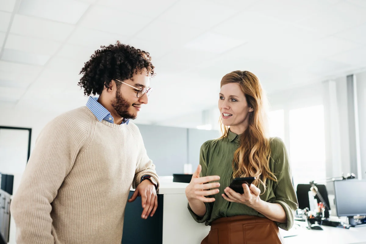 Office Manager Showing Colleague Something On Smartphone