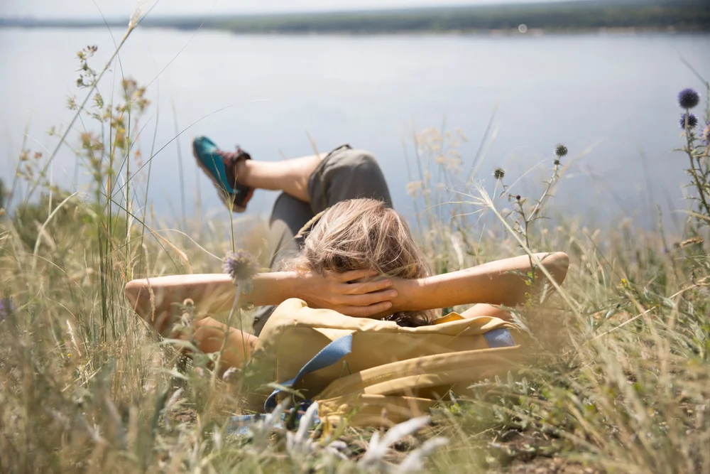 Woman with a backpack rests outdoors near a river