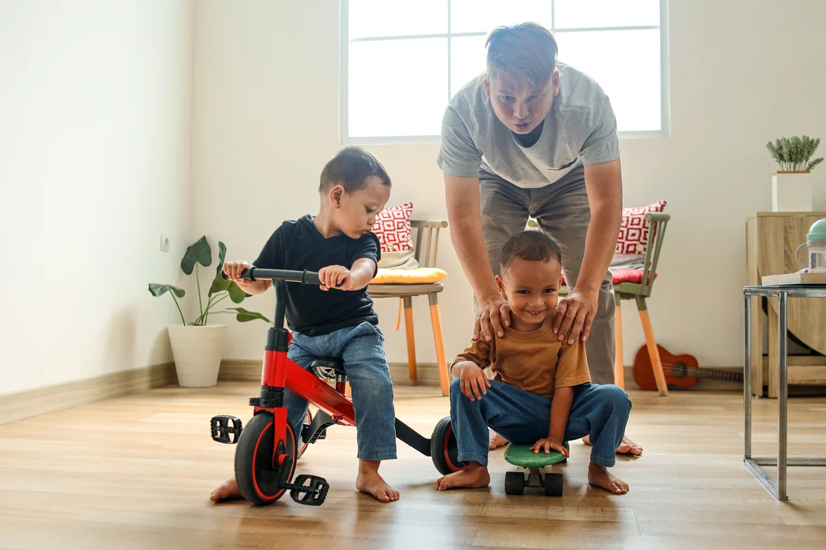 Children play with tricycle and skateboard with their father