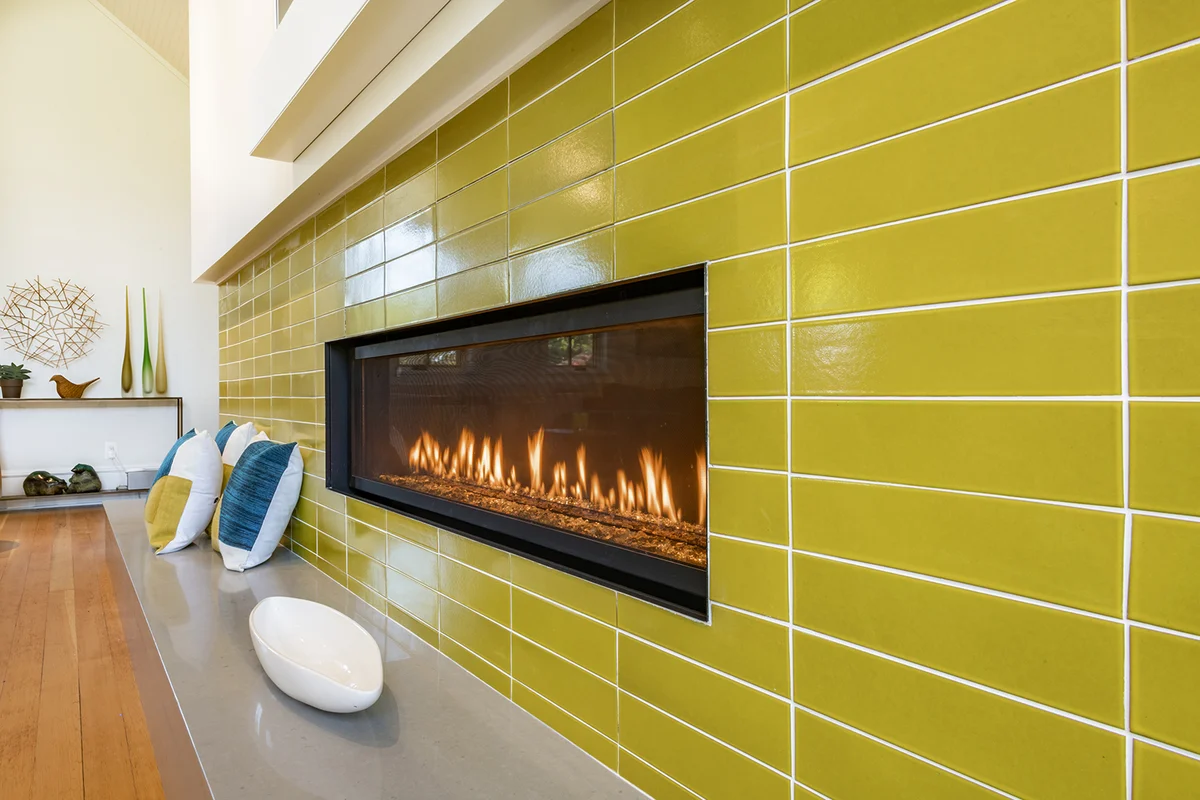 rectangular gas fireplace with chartreuse green tiles pillows flowers and steel art piece